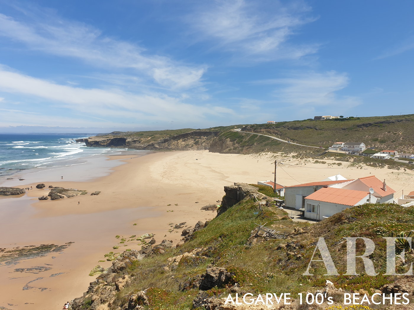 La playa de Monte Clérigo, vista de sur a norte, revela una pintoresca costa en forma de media luna adornada con casas. Cuando baja la marea, emergen formaciones rocosas en la playa.