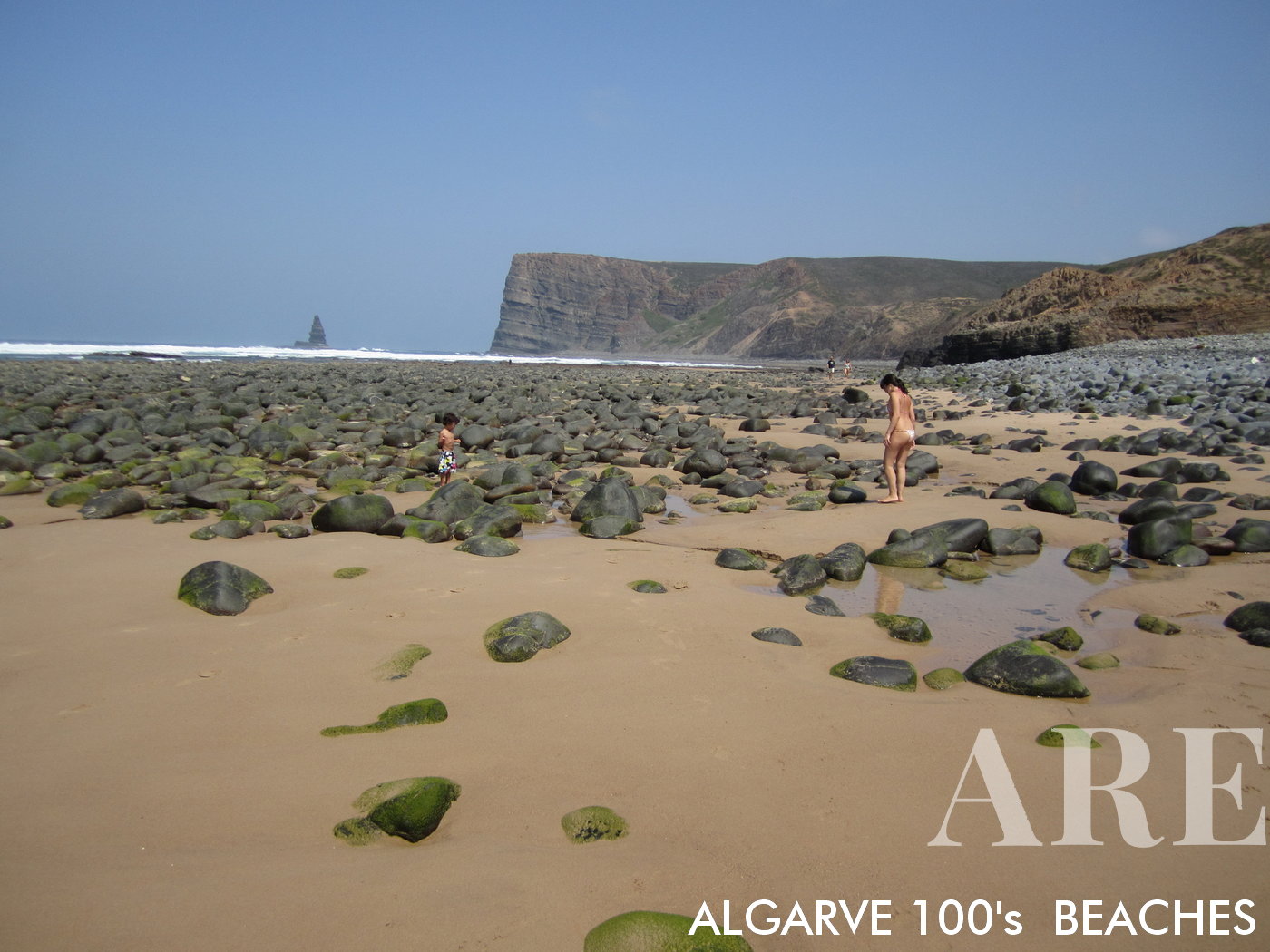 Canal Beach à Aljezur, en Algarve, présente un panorama enchanteur de petits rochers, de vagues rythmées et du vaste océan, culminant avec la silhouette distinctive du rocher de Ponta da Agulha à l'horizon.