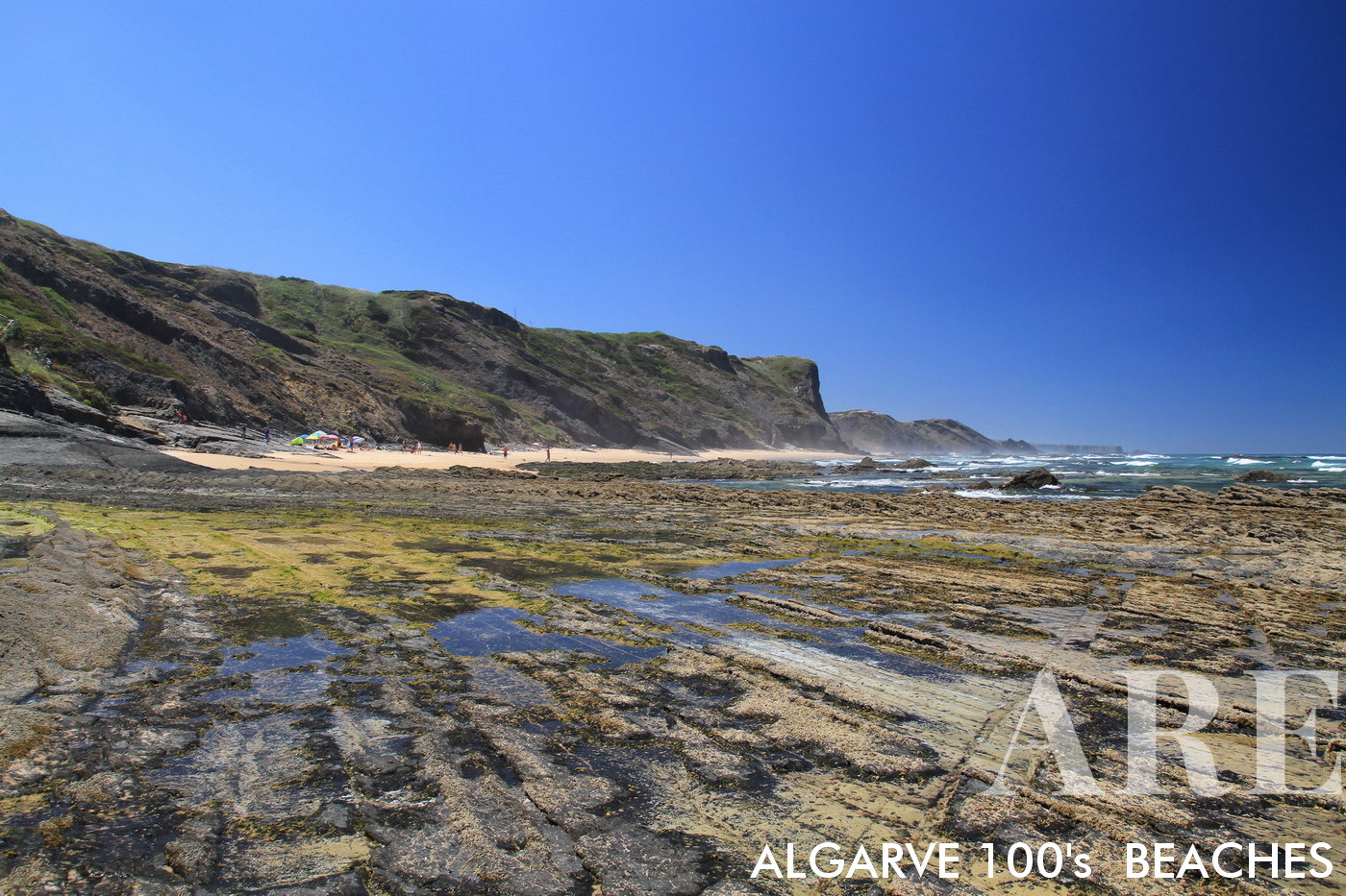 La playa de Carriagem en Rogil, Aljezur, Portugal, presenta una vista única de las formaciones rocosas en la playa durante la marea baja, acentuada aún más por los impresionantes acantilados que rodean este sereno lugar costero.