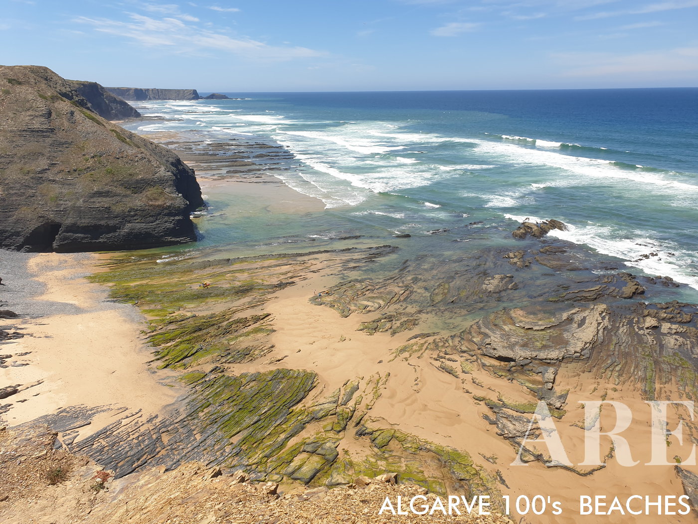 Southern view of Monte Clérigo Beach at low tide reveals a diverse landscape. The rocky formations, interspersed with smooth sand, foreground the commanding cliff views, presenting a captivating portrait of this coastal area.