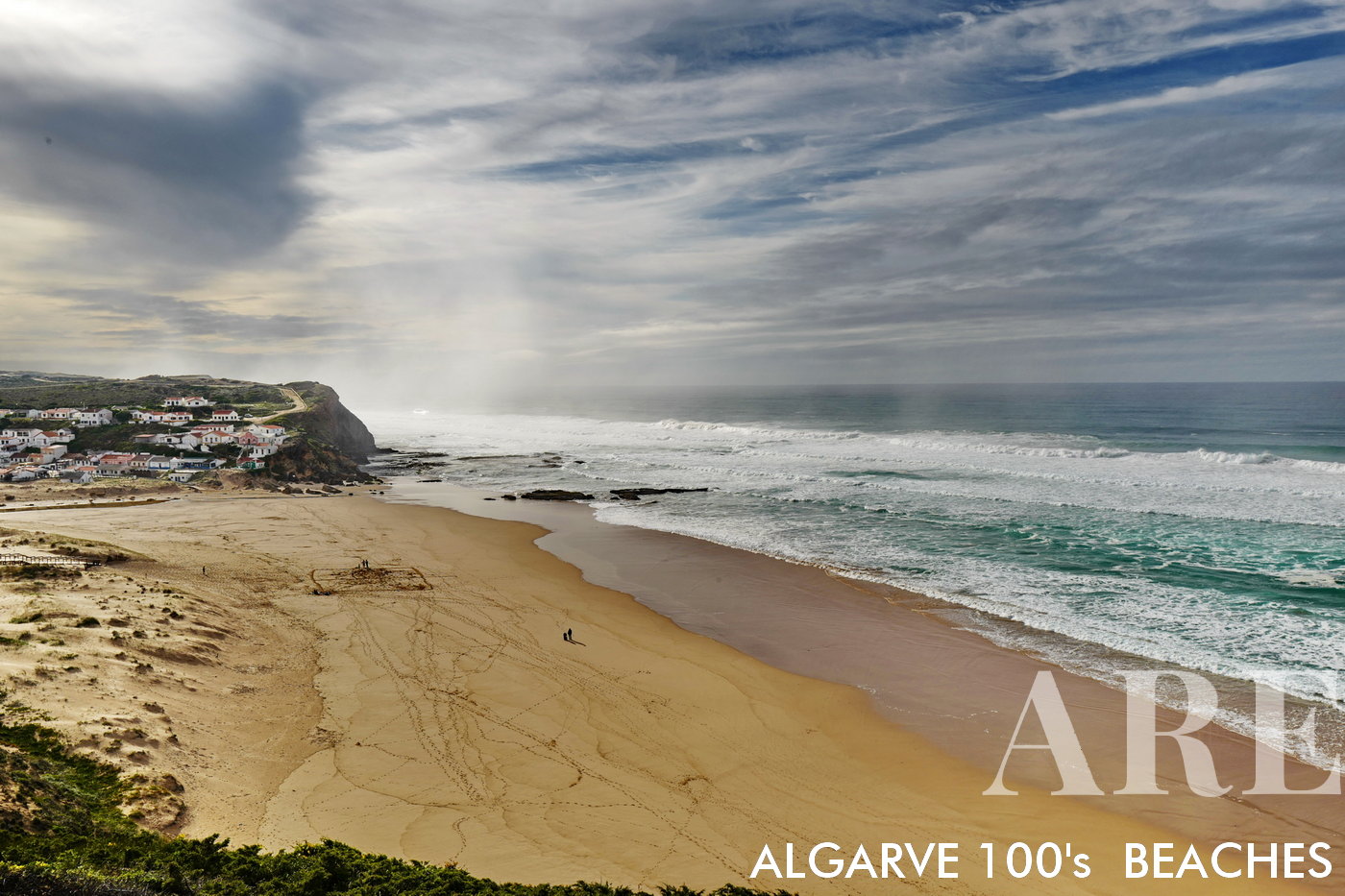 Winter at Monte Clérigo Beach in Algarve, Portugal presents a peaceful setting. The half-moon beach is bordered by a quaint village of houses, offering a scenic backdrop for a brisk walk along the shore.
