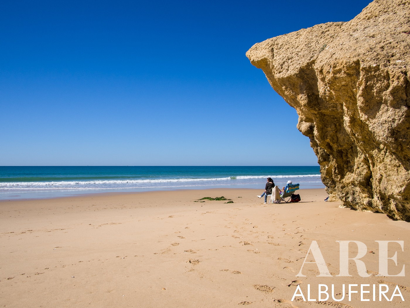 Escena cautivadora en Praia da Galé en marzo. Una imponente formación rocosa de piedra caliza a la derecha complementa perfectamente el cielo azul claro, creando una imagen llamativa.