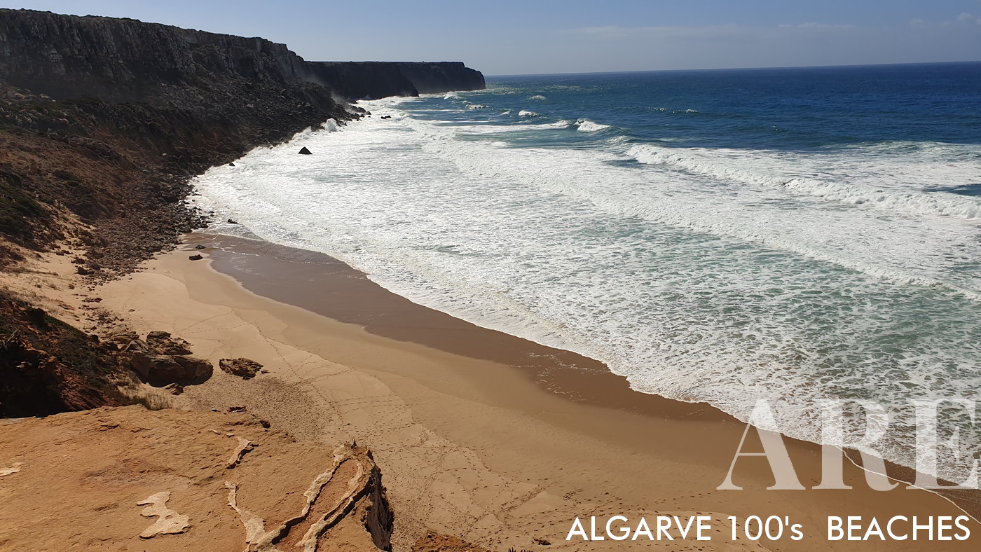 A Praia do Telheiro é envolta por arribas de rocha escura que formam uma barreira natural ao longo do areal.