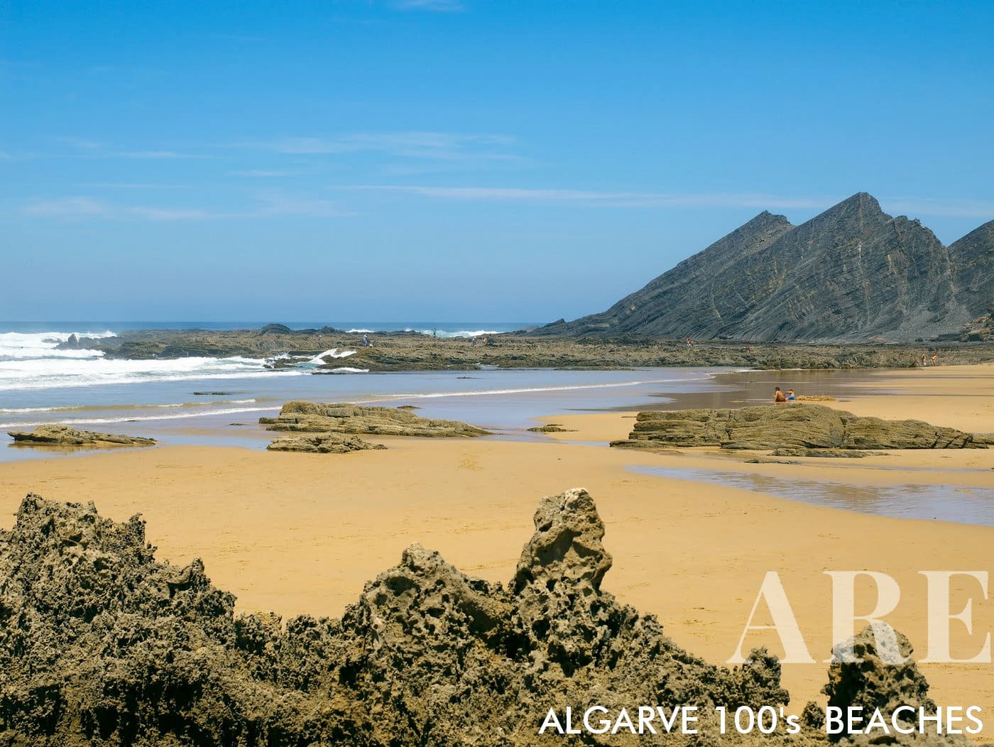 At Amoreira Beach in Algarve, Portugal, dramatic rock cliffs march towards the ocean, their grandeur mirrored by intriguing rock formations revealed on the sandy shore at low tide