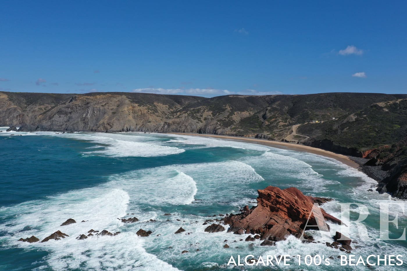 Captivating view of Ponta Ruiva Beach from the ocean, featuring the renowned Ruiva rock to the right, waves dancing from left to right, and a dramatic cliff gracing the right side of the image. A secretive surf haven, accessed only via a secluded dirt road.