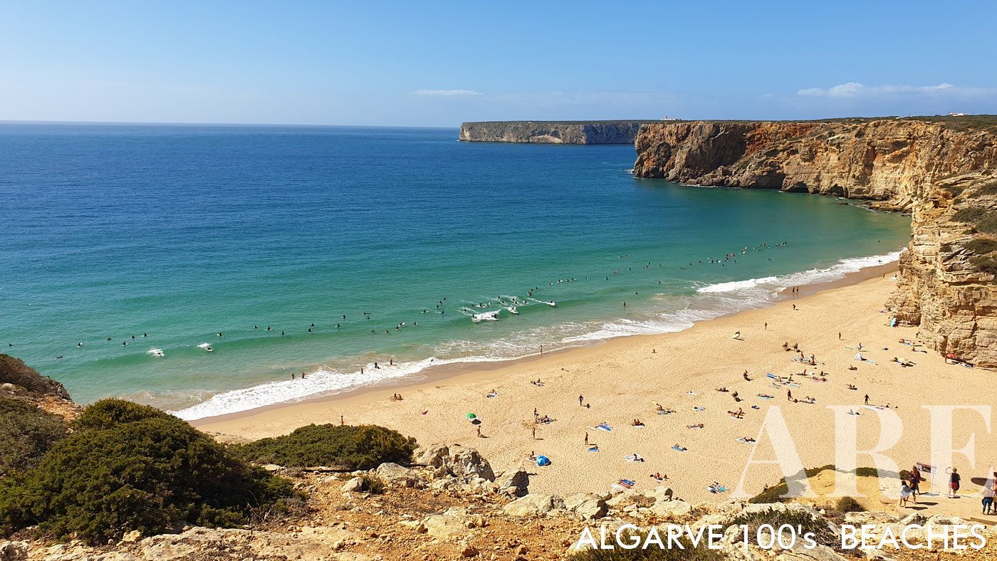 Commanding view from the top of the cliff over Beliche Beach, with the distant Farol de Cabo de Sao Vicente Lighthouse punctuating the horizon, creating a stunning tableau of Portugal